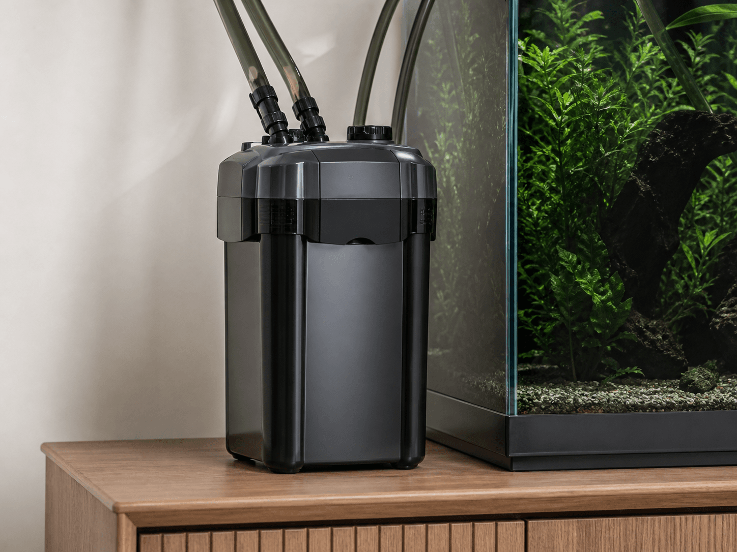 A sleek external canister filter placed beside a wooden aquarium cabinet.